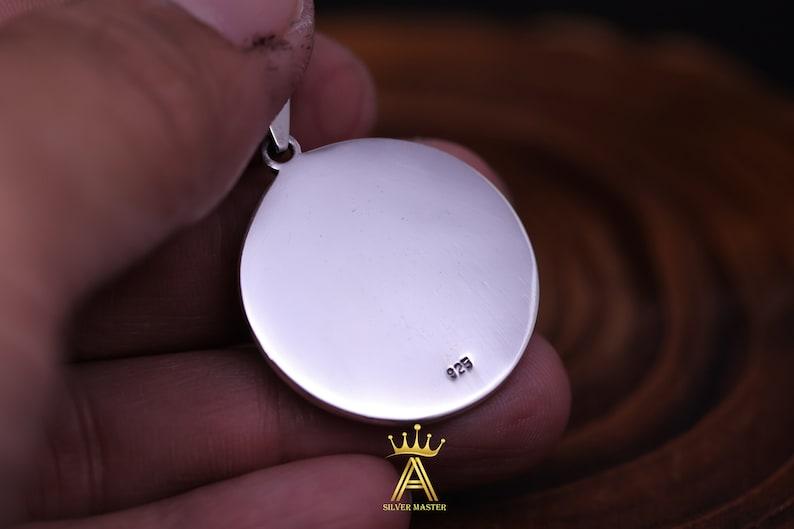 May include: A silver pendant with a round, smooth surface. The back of the pendant has the number "925" engraved on it.