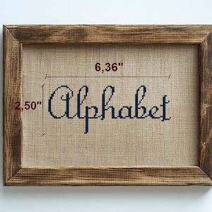 May include: A framed cross-stitch artwork with the word "Alphabet" in navy blue thread. The artwork is 6.36 inches wide and 2.50 inches high, set within a rustic, stained wooden frame. The background is a beige fabric.