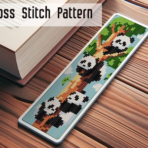 May include: A cross stitch bookmark featuring a white and black panda bear design. The panda is climbing a tree with green leaves. The bookmark is framed with a white border.