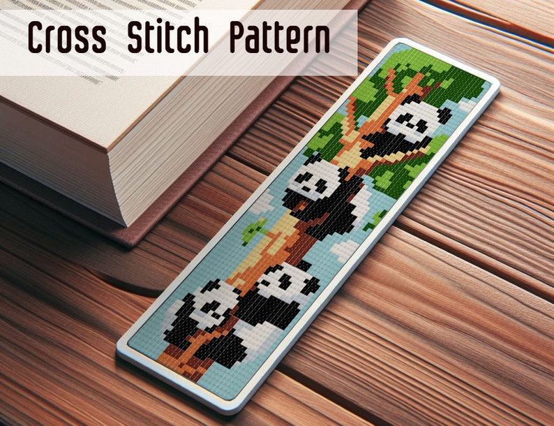 May include: A cross stitch bookmark featuring a white and black panda bear design. The panda is climbing a tree with green leaves. The bookmark is framed with a white border.