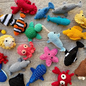Può includere: Una collezione di creature marine all'uncinetto, tra cui una stella marina, un polpo, un granchio, una balena, un delfino, un cavalluccio marino e altro ancora. I giocattoli sono realizzati in una varietà di colori, tra cui rosso, blu, verde, giallo e rosa.