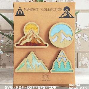 Può includere: Una collezione di calamite in legno a tema montagna su un cartoncino marrone. Le calamite presentano vari disegni, tra cui montagne, alberi e un sole. Il testo "MAGNET COLLECTION" e "HAND MADE" sono visibili. La parte inferiore del cartoncino include "SVG - PDF - DXF - EPS - CDR" e "DIGITAL DOWNLOAD".