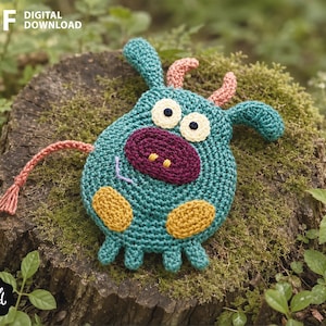 May include: A teal crochet creature with two pink horns, a large dark purple snout, two round cream-colored eyes with black pupils, and two yellow patches on its belly. It features a thin pink tail and four small teal legs.