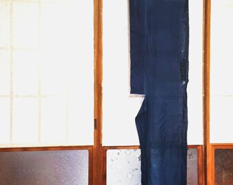 May include: A long, dark blue textile hanging from a wooden rod. The fabric appears to be a traditional Japanese garment, possibly a kimono or a similar item. The background features a traditional Japanese shoji screen.