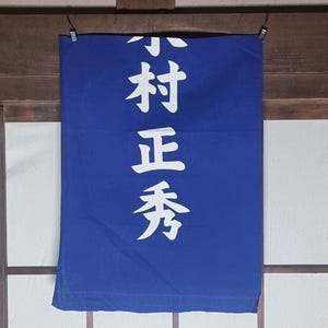 May include: A blue banner with white Japanese characters suspended from black clips. The vertically aligned text is likely a shop sign or decorative item.