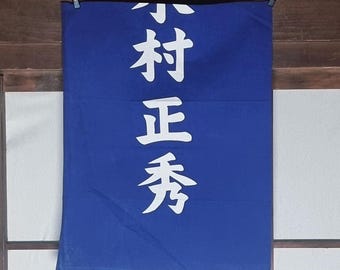May include: A blue banner with white Japanese characters hanging from black clips. The text is vertically oriented and appears to be a shop sign or decorative piece.