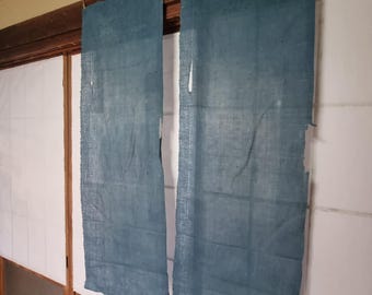 May include: Two rectangular, teal-colored fabric panels hang from a wooden beam. The panels have a raw, unfinished edge and are suspended in front of a traditional Japanese sliding door. The fabric appears to be linen or a similar natural fiber.