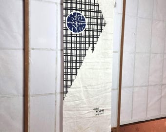 May include: A rectangular Japanese wall hanging with a wooden rod at the top. The design features a black and white checkered pattern on one side and a white fabric on the other. A blue circle with white calligraphy is centered on the checkered section.