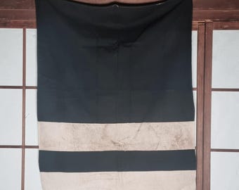 May include: A black and beige striped textile hanging against a wooden frame and a shoji screen. The top portion is solid black, with two beige stripes and a black stripe at the bottom. The textile is hanging from a black clip.