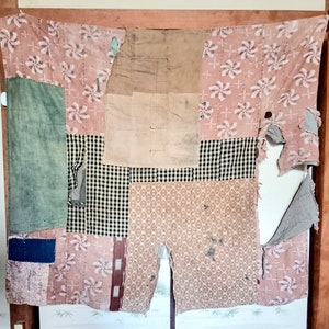 以下が含まれることがあります： ピンク、グリーン、ブラック、ホワイトの色合いの異なる生地で作られたパッチワークキルト。キルトは、縫い合わせられた生地の正方形と長方形で構成されています。キルトはいくつかの場所で破れており、下の生地が露出しています。