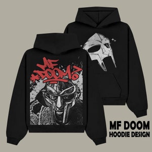 Puede incluir: Sudadera con capucha negra con un gráfico de la máscara de MF DOOM y el texto "MF DOOM" en estilo graffiti rojo.