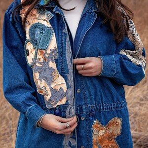 May include: A blue denim jacket with various fabric patches sewn on. The patches are in shades of blue, brown, and white. The jacket has a drawstring waist and a button closure.