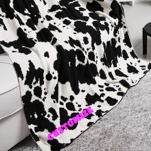 May include: Black and white cow print throw blanket with the word "CUSTOMIZE" in pink lettering on the bottom edge.