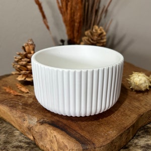 May include: White ceramic planter with a ribbed design. The planter is sitting on a wooden surface.