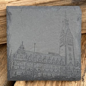 Könnte beinhalten: Ein schwarzes und weißes, graviertes Bild eines Gebäudes mit einem hohen Turm auf einem Schieferuntersetzer. Das Gebäude hat viele Fenster und eine detaillierte Fassade.