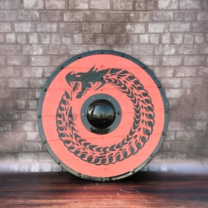 Könnte beinhalten: Ein runder, roter Schild mit einem schwarzen Drachenmuster. Der Drache ist um die Mitte des Schildes herumgewickelt, der einen schwarzen Kreis in der Mitte hat.