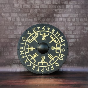 Könnte beinhalten: Ein runder schwarzer Schild mit goldenen Runen und Symbolen. Der Schild hat eine erhabene Mitte und ist mit einem Muster aus ineinandergreifenden Dreiecken und Kreisen verziert.