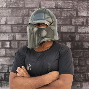 Op de afbeelding: Een persoon draagt een zwart T-shirt met een wit logo en een donkergrijze helm met een gezichtsmasker.