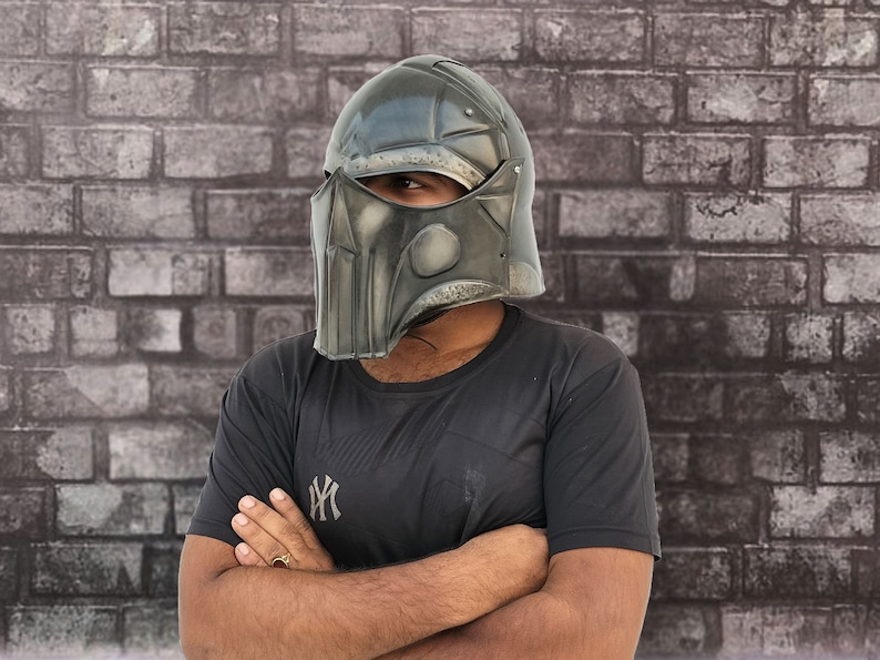 Op de afbeelding: Een persoon draagt een zwart T-shirt met een wit logo en een donkergrijze helm met een gezichtsmasker.