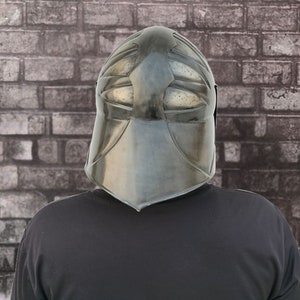 Op de afbeelding: Een persoon draagt ​​een zwarte helm met een gezichtsbeschermer en een zwart shirt.