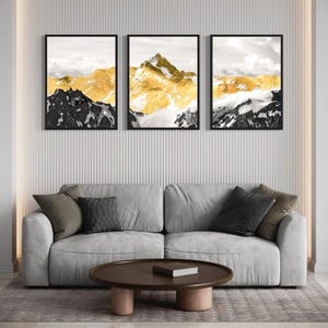 Może przedstawiać: Trzy czarne oprawione wydruki górskiego krajobrazu pokrytego śniegiem z złotymi akcentami. Wydruki wiszą na białej ścianie z pionowymi żłobieniami.