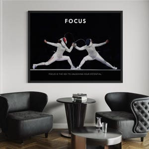 May include: A framed print with a black background showing two fencers in white, poised for action. The word "FOCUS" is at the top, with the text "FOCUS IS THE KEY TO UNLOCKING YOUR POTENTIAL" at the bottom. The print is displayed in a room with black chairs.