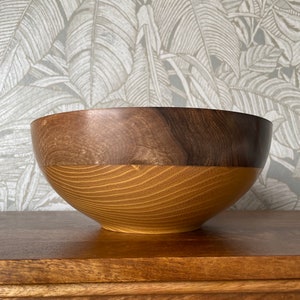 May include: A wooden bowl with a dark brown top and a light brown bottom. The bowl is made from two different types of wood.