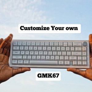 Könnte beinhalten: Eine weiße mechanische Tastatur mit dem Text "Customize Your Own" und "GMK67" auf dem Bildschirm. Die Tastatur wird von zwei Händen vor einem blauen Himmel gehalten.