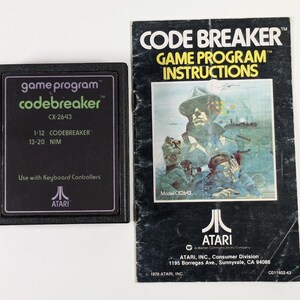May include: A black Atari game cartridge with the text "game program codebreaker CX-2643 1-12 CODEBREAKER 13-20 NIM" and the Atari logo. The cartridge is next to a black and white instruction booklet with the text "CODE BREAKER GAME PROGRAM INSTRUCTIONS" and a picture of a man in a hat.