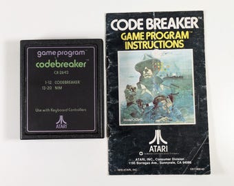 May include: A black Atari game cartridge with the text "game program codebreaker CX-2643 1-12 CODEBREAKER 13-20 NIM" and the Atari logo. The cartridge is next to a black and white instruction booklet with the text "CODE BREAKER GAME PROGRAM INSTRUCTIONS" and a picture of a man in a hat.