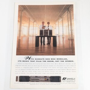 May include: A vintage advertisement for Sansui's new mini modular stereo system. The ad features two men standing in a large, white, open space, holding the stereo components. The text reads "With Sansui's new mini modular, it's music that fills the room, not the stereo." The ad also includes the Sansui logo and the tagline "Engineered to fit your life."