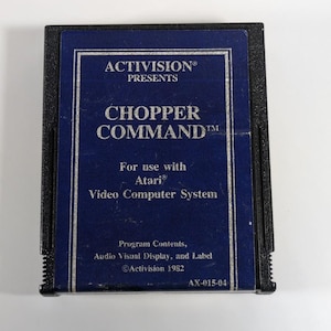 May include: A vintage Atari video game cartridge for "Chopper Command" by Activision. The cartridge has a dark blue label with white text and a black plastic casing. The label includes the game title, company information, and Atari compatibility.