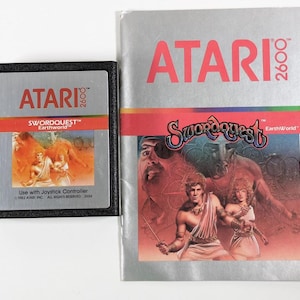 May include: A vintage Atari 2600 game cartridge and instruction manual for Swordquest: Earthworld. The cartridge is black with a red and white label featuring the game title and Atari logo. The manual is silver with a red and white label featuring the game title and Atari logo.