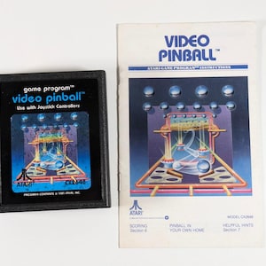 May include: A black Atari Video Pinball cartridge and instruction manual. The cartridge has the game title and a graphic of a pinball machine. The manual features the game title and a pinball machine graphic. The Atari logo is visible.