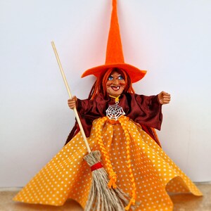 May include: A handmade witch doll with orange and brown clothing, a tall orange hat, and a broom. The doll has a white spiderweb pendant and a polka dot skirt.