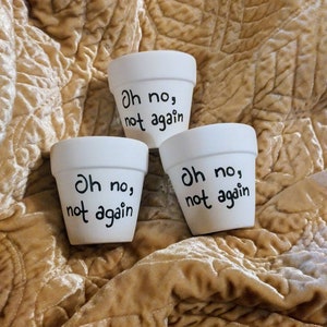 May include: Three white ceramic flower pots with black lettering that reads "Oh no, not again".