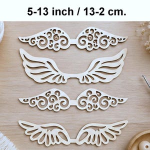 Puede incluir: Cuatro recortes de madera de color claro en forma de alas dispuestos en dos pares. Dos alas presentan intrincados patrones de filigrana en espiral, mientras que dos alas tienen diseños de plumas simples y limpios. El texto 13-2 cm aparece arriba.