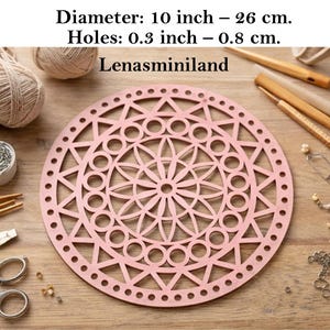 Può includere: Base in legno rosa tagliata al laser con un design geometrico, con un motivo floreale centrale e triangoli e cerchi circostanti. Il diametro è di 26 cm, i fori di 0,8 cm. Il testo "Lenasminiland" è visibile.