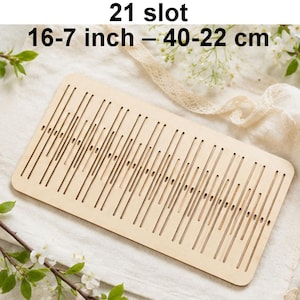 May include: A light-colored wooden weaving tool with 21 slots. The tool measures 16-7 inches in length. The slots are evenly spaced and run the length of the rectangular piece of wood. The text "21 slot" and "16-7 inch - 40-22 cm" are printed at the top.