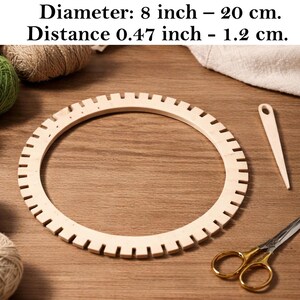 Pode incluir: Um tear circular de madeira clara com entalhes espaçados uniformemente ao longo da borda externa. O tear tem um diâmetro de 20 cm e uma distância entre entalhes de 1,2 cm. Uma agulha de madeira e uma tesoura de metal estão presentes.