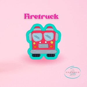 Puede incluir: Un cortador de galletas de camión de bomberos rojo con un contorno turquesa. El cortador de galletas tiene la forma de la parte delantera de un camión de bomberos con faros, parabrisas y parrilla.