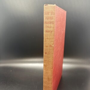 May include: A red hardcover book with a spine that reads "Not By Arms Alone" by John  .