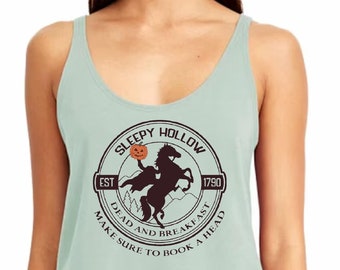 May include: A light green tank top with a round neckline. The front features a circular graphic with the words "Sleepy Hollow" and "Dead and Breakfast" surrounding an image of the Headless Horseman. The text "Make sure to book a head" is also included.