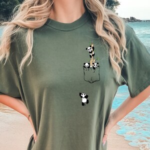 May include: A green t-shirt with a pocket featuring a graphic of three pandas climbing a bamboo stalk. A fourth panda is peeking out from the pocket.