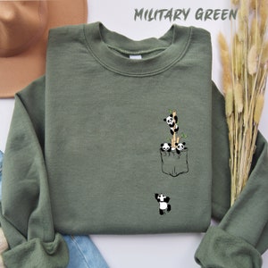 May include: A military green sweatshirt with a pocket featuring a graphic of four pandas climbing bamboo stalks. The text "MILITARY GREEN" is printed in white at the top of the image.