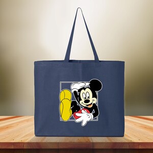May include: Navy blue tote bag featuring a graphic of Mickey Mouse in a white square. The cartoon character is black, white, red, and yellow. The bag has two navy blue handles and is made of a sturdy fabric.