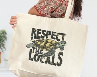 May include: Cream-colored tote bag featuring a sea turtle illustration and the text "Respect the Locals" in a distressed black font. The bag has a rectangular shape with long straps for carrying over the shoulder.