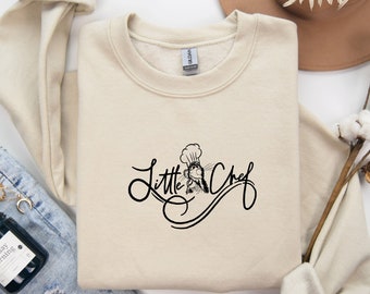 May include: A beige sweatshirt with a black graphic of a cartoon chef with the text "Little Chef" in a cursive font.