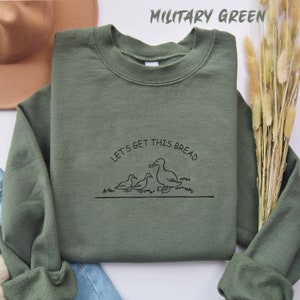 May include: A military green sweatshirt with the text "Let's get this bread" and a graphic of three ducks walking in a line.
