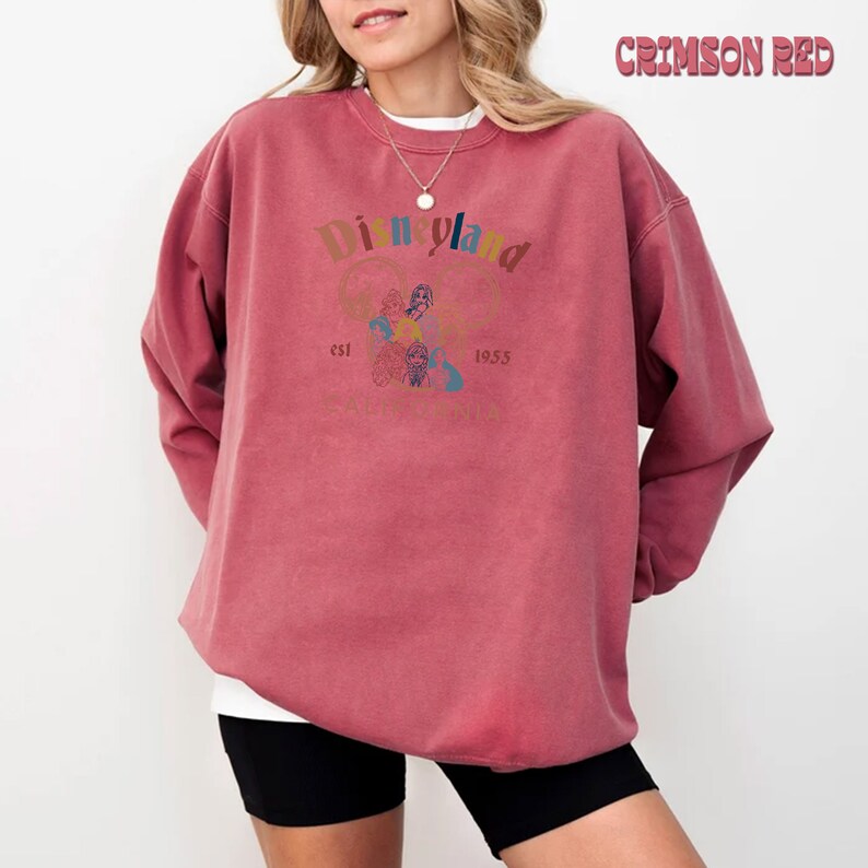 May include: A crimson red sweatshirt with a vintage-style Disneyland logo featuring the iconic Mickey Mouse ears and the text "Disneyland est. 1955 California".